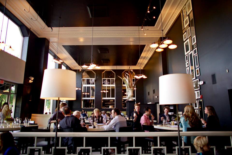 Guests seated inside the main dining room at Easy Bistro, a great place to eat in downtown Chattanooga, which features tall ceilings, dark painted walls, large windows, and warm lighting with modern fixtures.