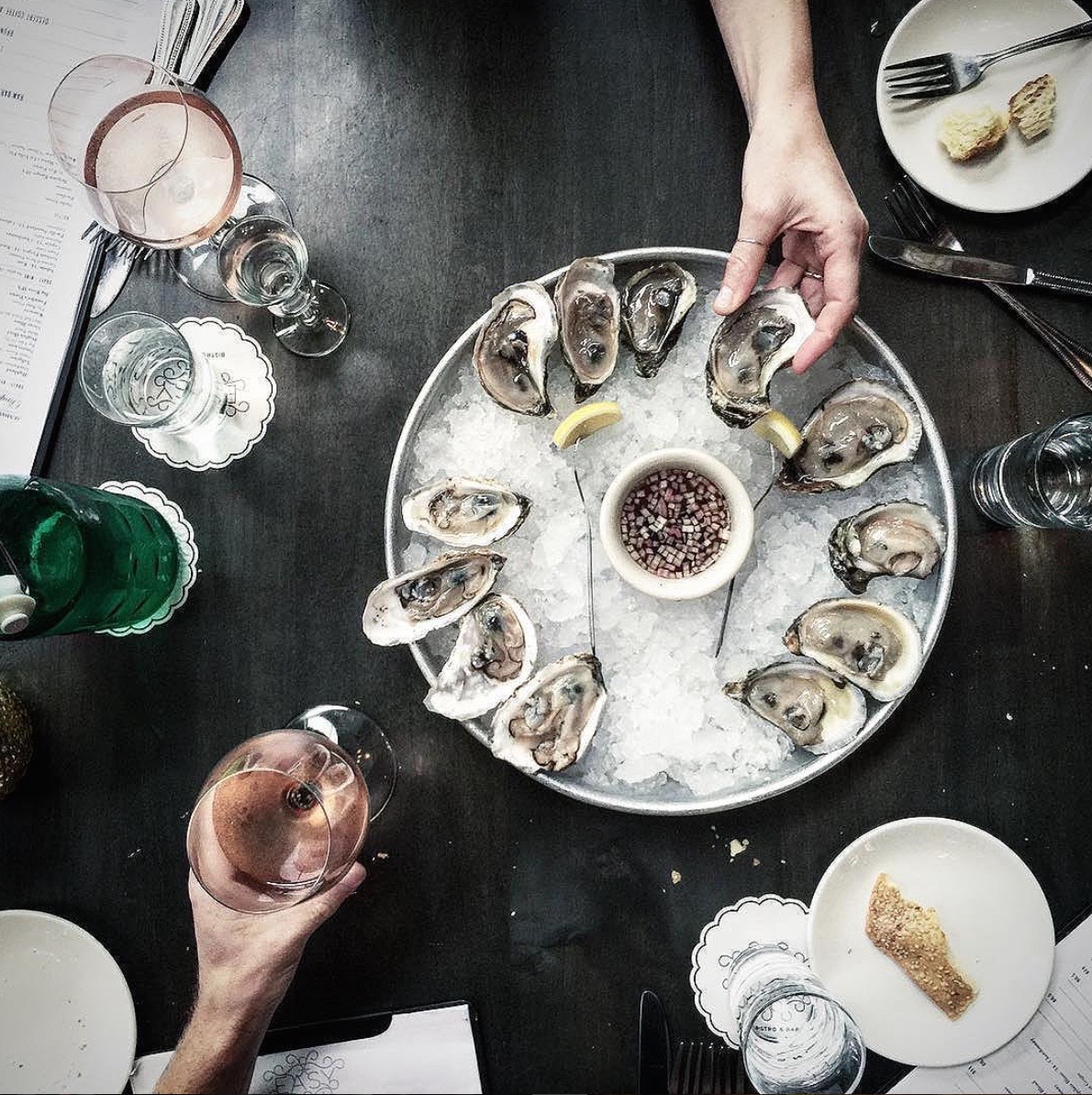 Overhead view of a seafood platter with oysters on ice, lemon wedges, and drinks at Easy Bistro, ideal for an anniversary dinner restaurant near me
